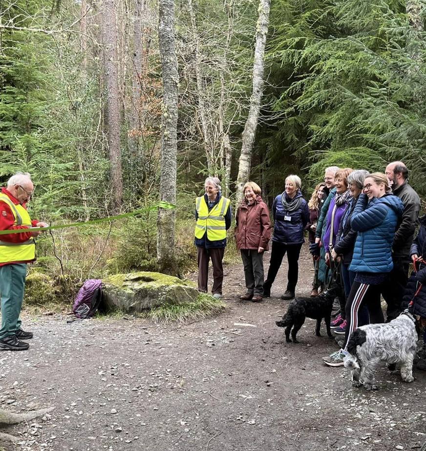 A man cuts a ribbon to formally open a stretch of new accessible pathway at Banchory as a crowd of supporters look on. 