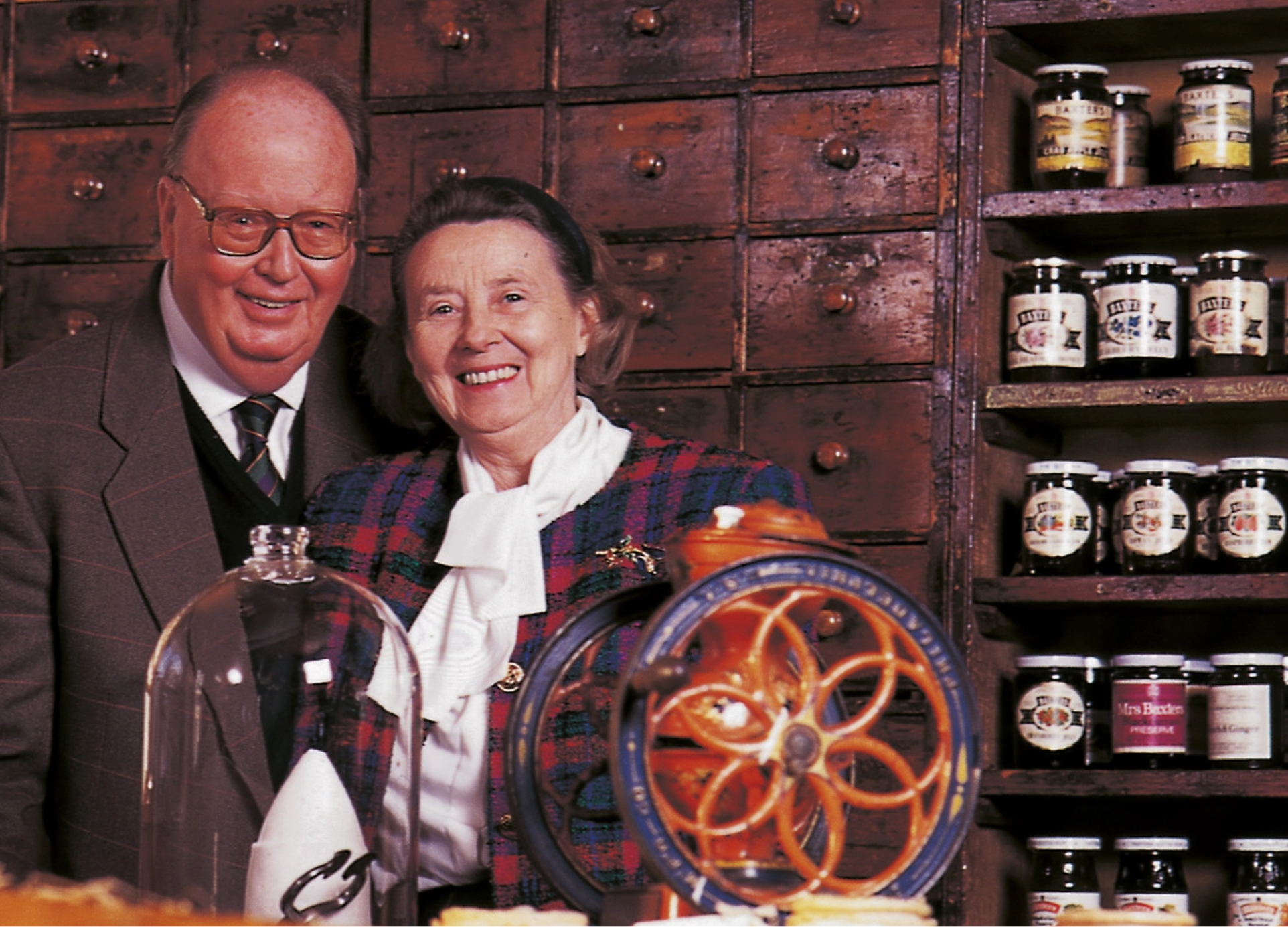 Gordon and Ena Baxter pictured in a store, with jars of Baxters preserves in the background. 